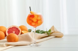 Ein Glas alkoholfreier Aperol Spritz mit Eiswürfeln und Orangenscheiben, daneben angeschnittene Zitrusfrüchte.