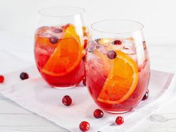Zwei Gläser mit Cranberry-Orangen-Spritz stehen auf einer weißen Serviette. Als Dekoration liegen einige Cranberrys neben den Gläsern.