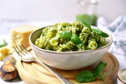 Eine Schüssel Feta-Spinat-Pasta garniert mit frischem Basilikum und Parmesan, auf einem Brett, daneben eine Gabel.