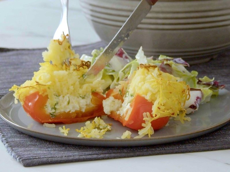 Eine angeschnittene gefüllte Paprika mit Kartoffelhaube und Feta gefüllt auf einem Teller.