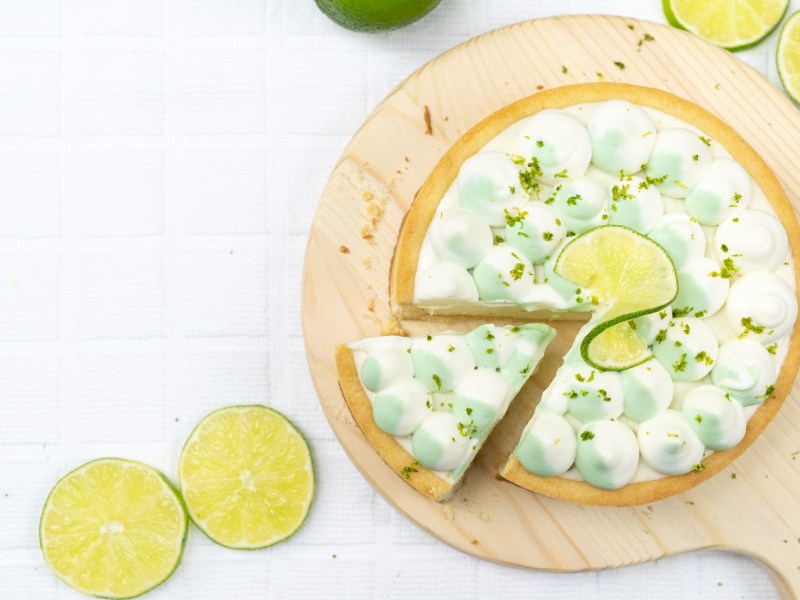 Gin-Tonic-Kuchen in der Draufsicht, auf einem Brett, ein Stück ist schon angeschnitten, verziert mit Limetten.