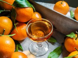 Mandarinenlikör in einem kleinen Glas serviert. Außen herum liegen Mandarinen als Dekration.