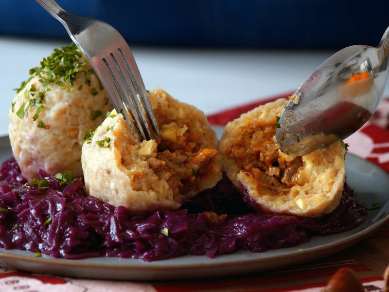 Zwei Maronenknödel mit Entenfüllung auf einem Teller mit Rotkohl. Einer der Knödel wurde aufgeschnitten, um die Füllung zu präsentieren.