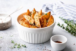 Eine weiße Schale Paprika-Kartoffeln mit Kräutern bestreut, daneben Kräuterzweige und eine Schale mit Gewürz.