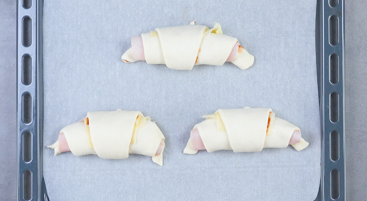 Drei Pizza-Croissants auf einem mit Backpapier belegten Blech.