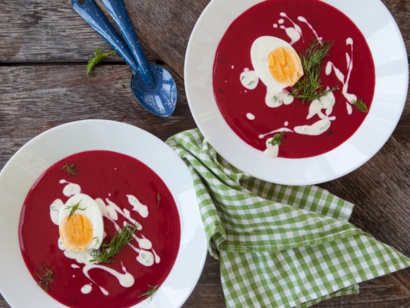 Zwei Schüsseln mit Rote-Bete-Suppe. Daneben ein Geschirrtuch und Löffel.