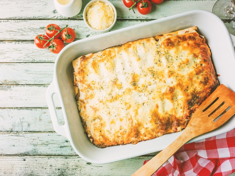 Sauerkraut-Lasagne in Auflaufform, darauf ein Holzlöffel, drumherum Tomaten und Käse, Draufsicht.