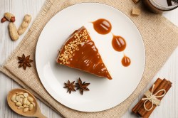 Ein Stück Spekulatius-Cheesecake mit Karamellsoße und Nüssen auf einem Teller, Draufsicht, daneben Anissterne und weihnachtliches Zubehör.