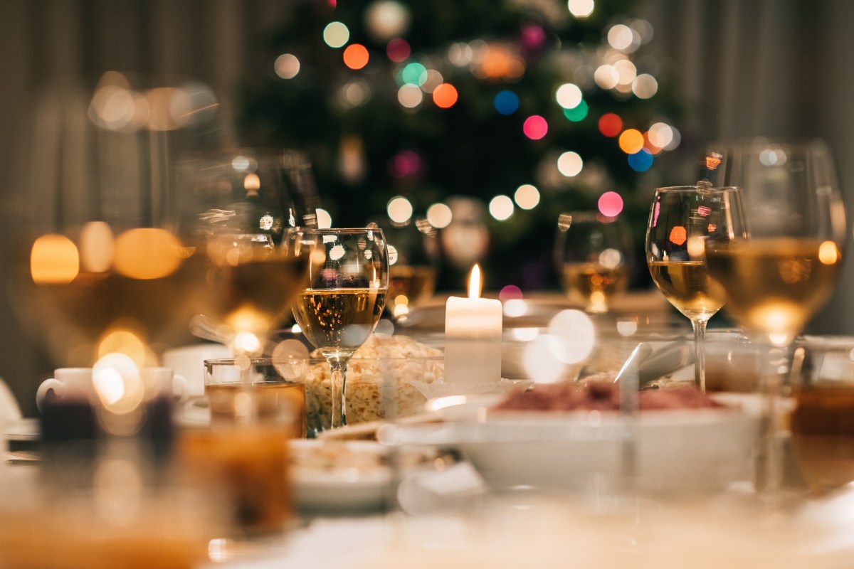 Was essen die Deutschen zu Weihnachten: ein weihnachtlich gedeckter Tisch, im Hintergrund unscharf ein erleuchteter Tannenbaum.