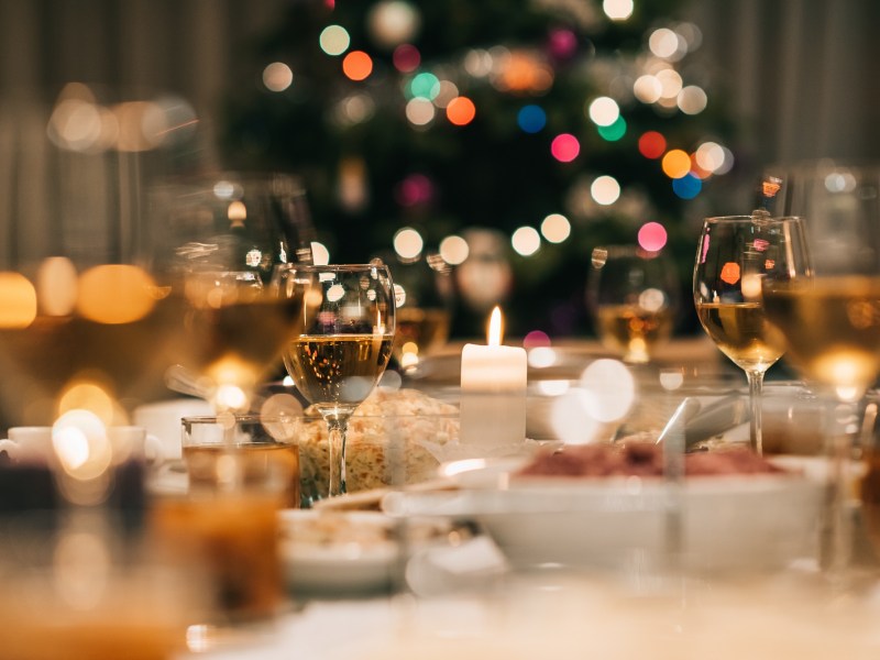 Was essen die Deutschen zu Weihnachten: ein weihnachtlich gedeckter Tisch, im Hintergrund unscharf ein erleuchteter Tannenbaum.