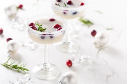 2 Gläser White Christmas Margarita mit Kokosrand und frischen Cranberrys garniert, daneben Weihnachtsdeko und Cranberrys.