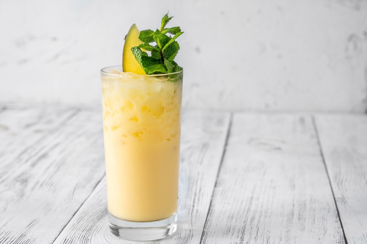 Ein Glas Alkoholfreier Mango-Cocktail mit Eis, garniert mit Minze und einer Mangospalte.