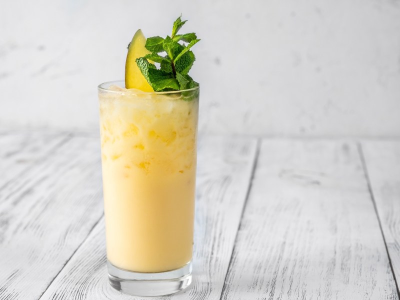Ein Glas Alkoholfreier Mango-Cocktail mit Eis, garniert mit Minze und einer Mangospalte.