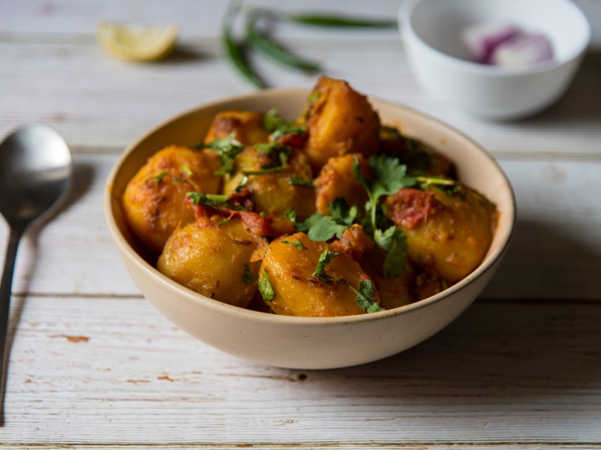 Eine Schale Aloo Masala, also Bombay-Katoffeln, mit Petersilie bestreut, daneben ein Löffel.