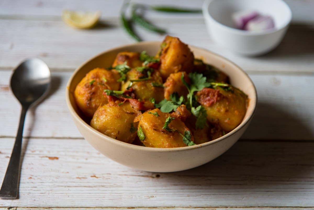 Eine Schale Aloo Masala, also Bombay-Katoffeln, mit Petersilie bestreut, daneben ein Löffel.