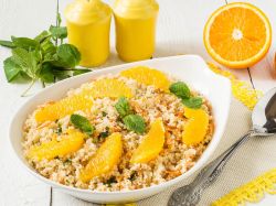 Bulgur-Orangen-Bowl, serviert in einer Schüssel. Orangenscheiben und Minze als Deko. Salz- und Pfefferstreuer sowie frische Minze und eine aufgeschnittene Orange stehen als Dekoration neben und hinter der Schüsse.