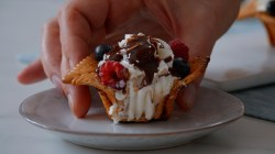 Ein angebissener Butterkeks-Muffin mit Vanillesahne, Beeren und Schokosoße, der auf einen Teller gesetzt wird.