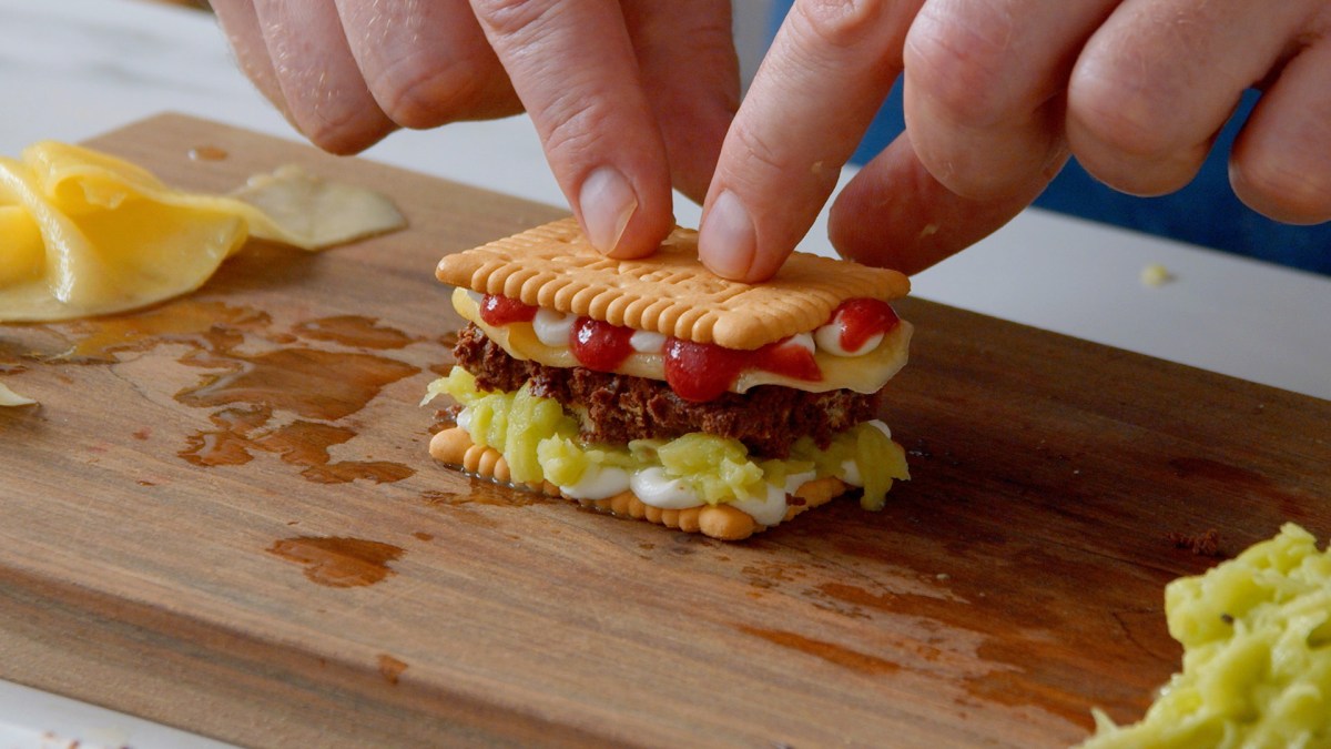 Ein kleines Butterkeks-Sandwich mit Sahne, Obst, Himbeersoße und Schokolade auf einem Brett.