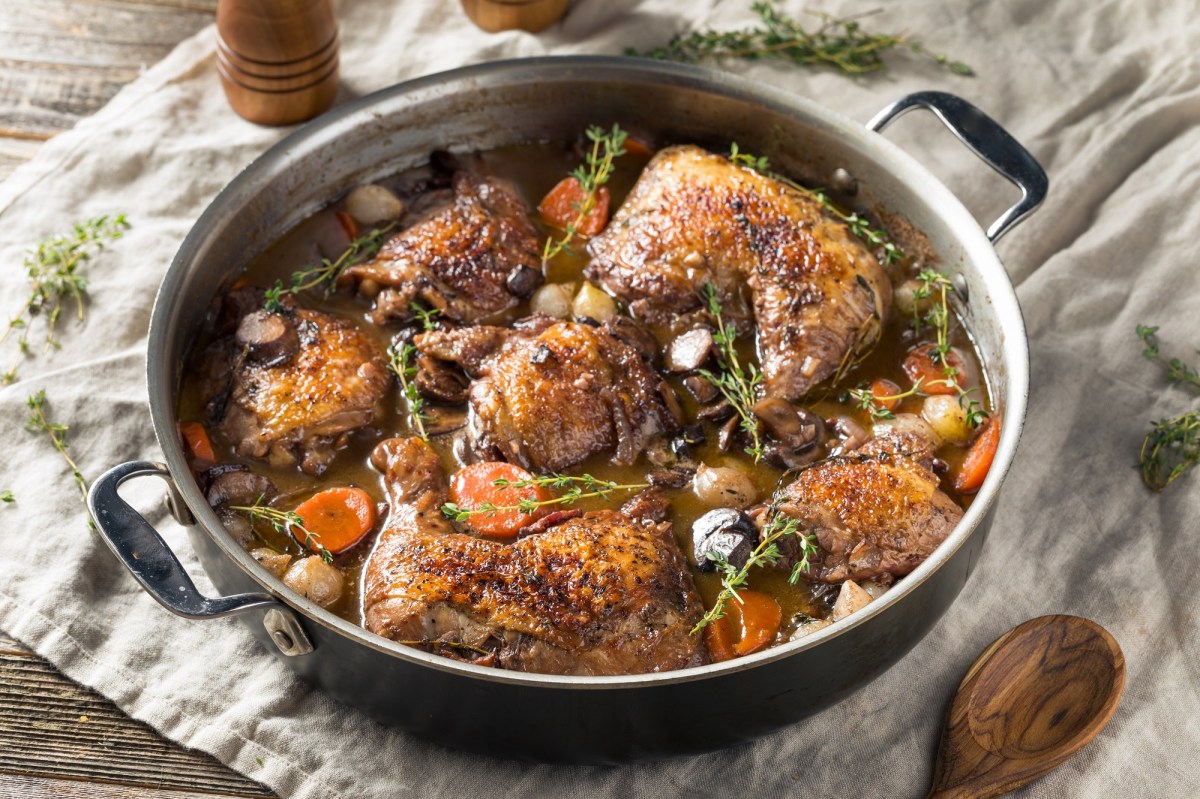 Coq au Vin mit Thymian garniert in einer gusseisernen Pfanne auf einem grauen tuch.