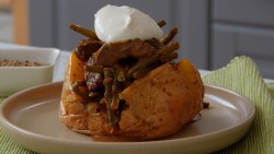 Eine gefüllte Ofenkartoffel mit Bohnenragout und einem Klecks Schmand auf einem Teller.