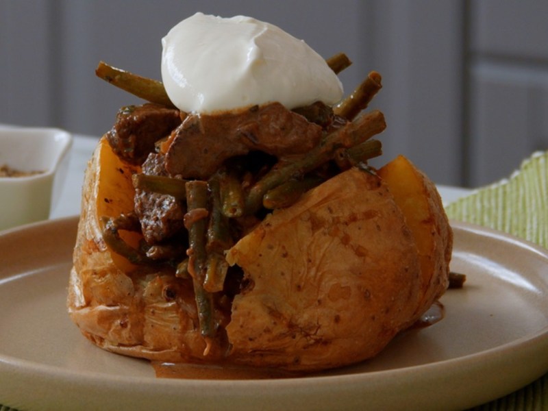 Eine gefüllte Ofenkartoffel mit Bohnenragout und einem Klecks Schmand auf einem Teller.