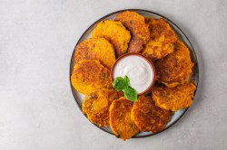 Ein Teller Hash Browns, fächerartig im Kreis angeordnet, in der Mitte eine Schale weißer Dip.