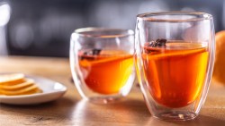 2 Gläser Hot Aperol mit Orangenscheiben und winterlichen Gewürzen. Daneben steht eine schale mit Orangenscheiben.