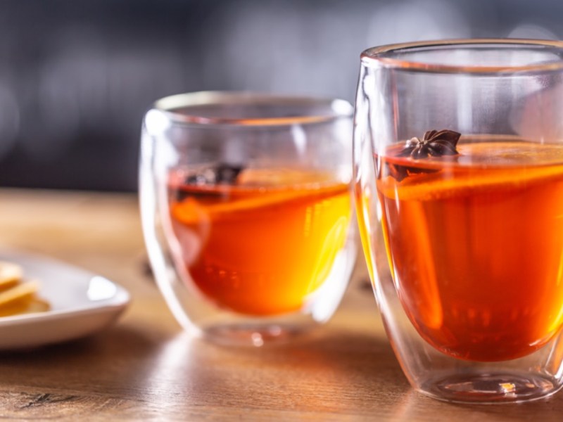2 Gläser Hot Aperol mit Orangenscheiben und winterlichen Gewürzen. Daneben steht eine schale mit Orangenscheiben.
