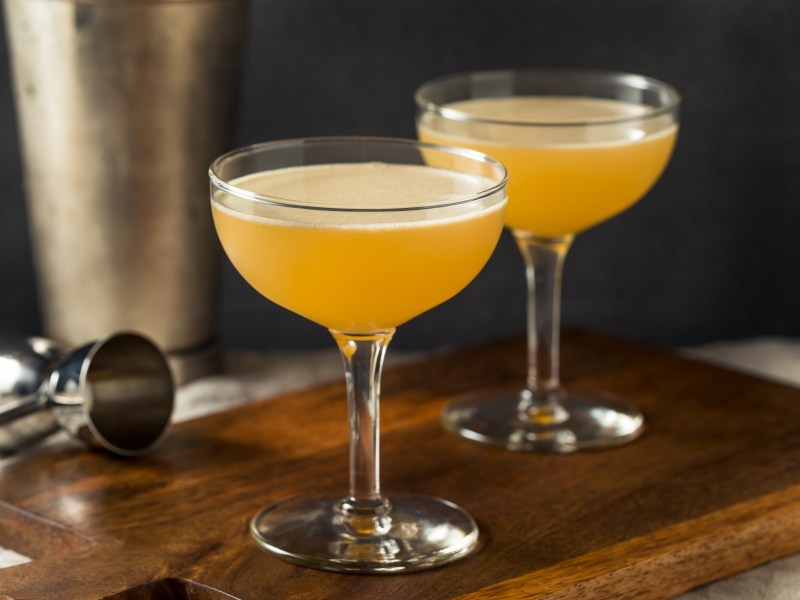 2 Gläser Italian Martini auf einem Brett, daneben ein Cocktailshaker und ein Bar-Messbecher.