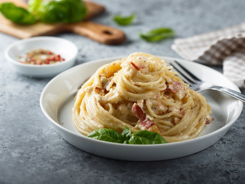 Italienische Carbonara auf einem weißen Teller, garniert mit Basilikum.