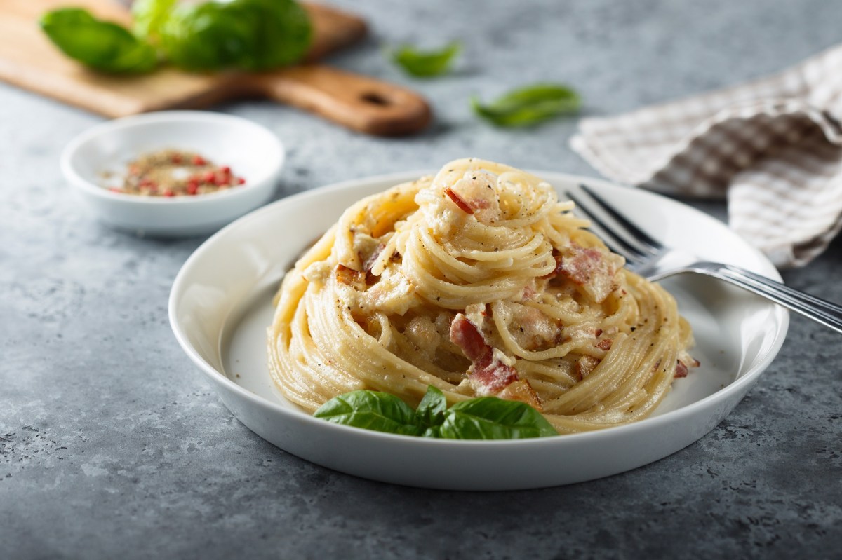 Italienische Carbonara auf einem weißen Teller, garniert mit Basilikum.