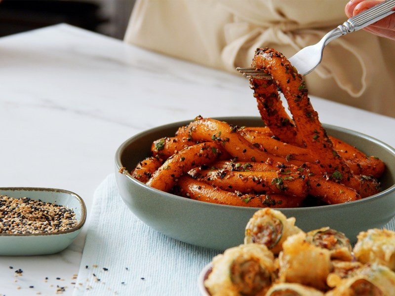 Ein Teller Kartoffelnudeln, daneben eine Schale mit frittierten Zucchini-Röllchen und eine Schale Sesam.