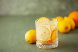 Ein Glas Limoncello Tonic mit Eiswüfeln und Zitronenscheiben, dahinter frische Zitronen.
