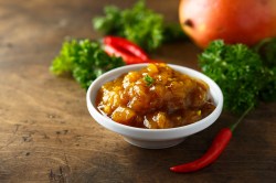 Mango-Chutney in einer kleinen Schale auf, dekoriert mit Chilis und Petersilie.