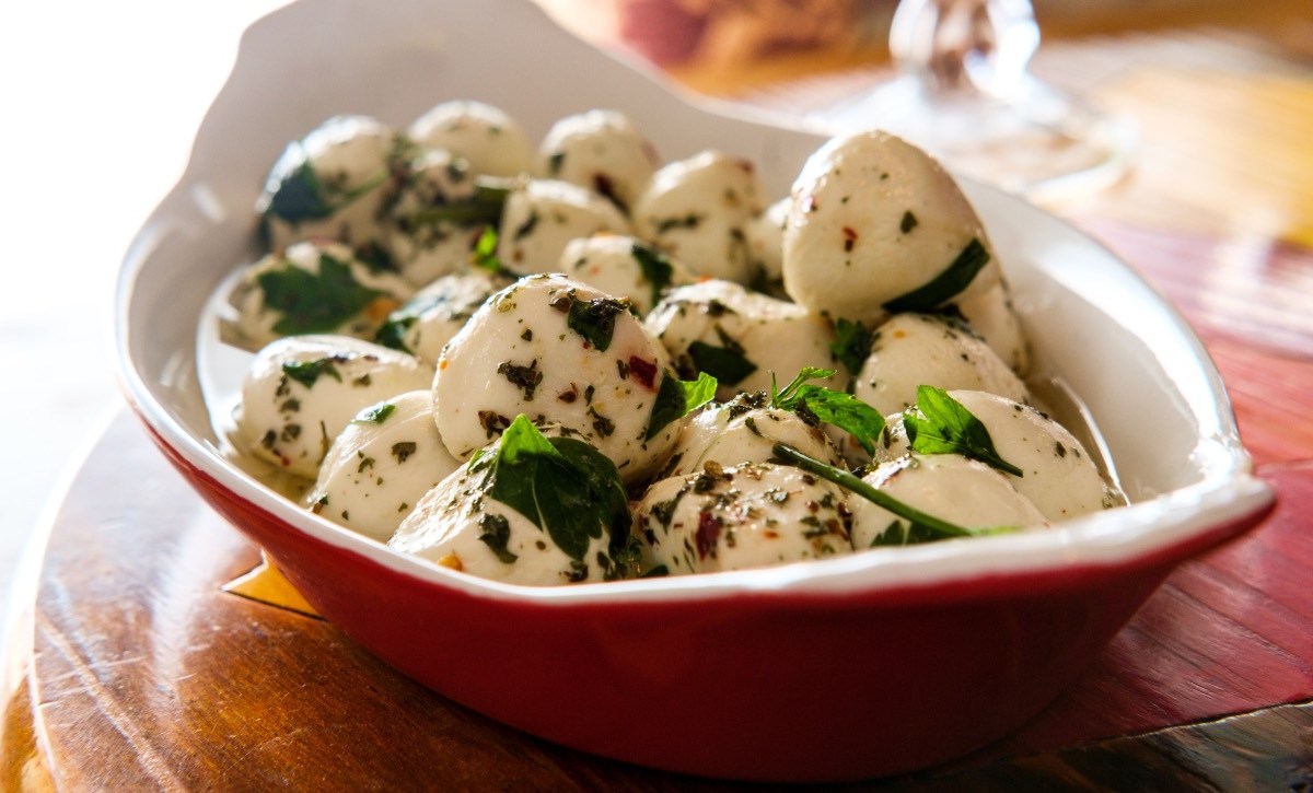 Eine rote Schale voller mariniertem Mozzarella mit Kräutern.