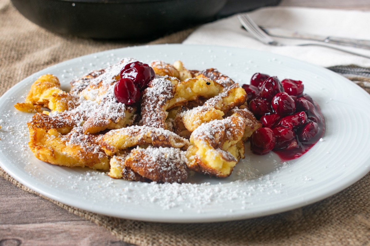 Österreichischer Kaiserschmarrn auf einem weißen Teller, serviert mit Kirschen und Puderzucker