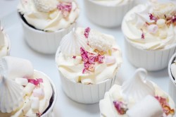 Prosecco-Cupcakes auf einem weißen Untergrund, dekoriert mit Rosenblättern, Marshmallows und Baiser.