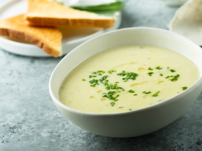 Eine Schüssel Schwarzwurzelsuppe mit frischem Schnittlauch. Daneben ein Teller mit 2 halbierten Toastscheiben.