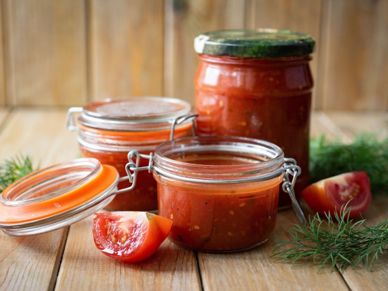 drei Gläser selbstgemachter Ketchup mit Tomaten und Dill garniert.