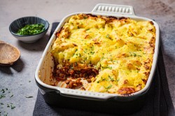 Shepherd's Pie mit Hack und Kartoffelbrei in einer Auflaufform mit Petersilie bestreut, ein Stück ist schon weg