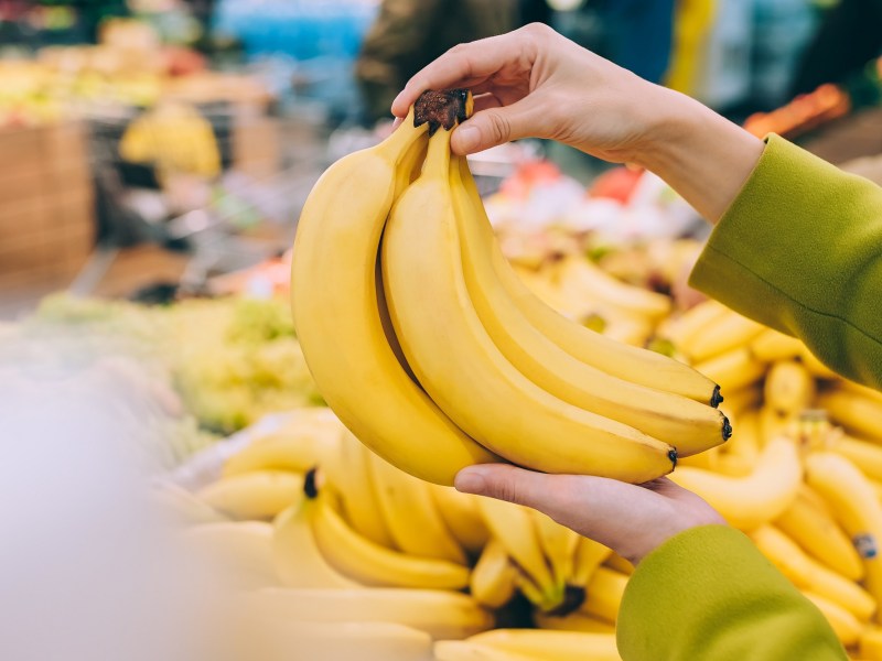 So bleiben Bananen länger frisch: Eine Frau hält ein paar Bananen in der Hand, man sieht nur ihre Hände.