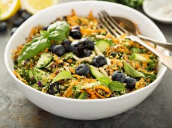 Eine Schüssel Superfood-Salat mit Blaubeeren, Gurke, Möhren, Avocado und weiteren Zutaten, darin Gabel und Löffel, Nahaufnahme.