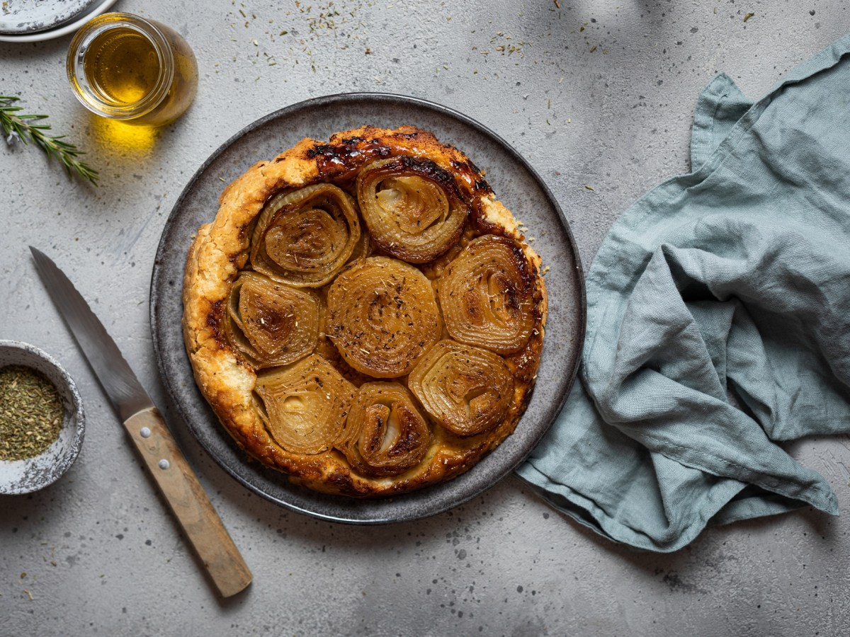 Tarte Tatin mit Zwiebeln auf einem blauen Teller, daneben Olivenöl und Rosmarin