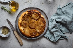 Tarte Tatin mit Zwiebeln auf einem blauen Teller, daneben Olivenöl und Rosmarin