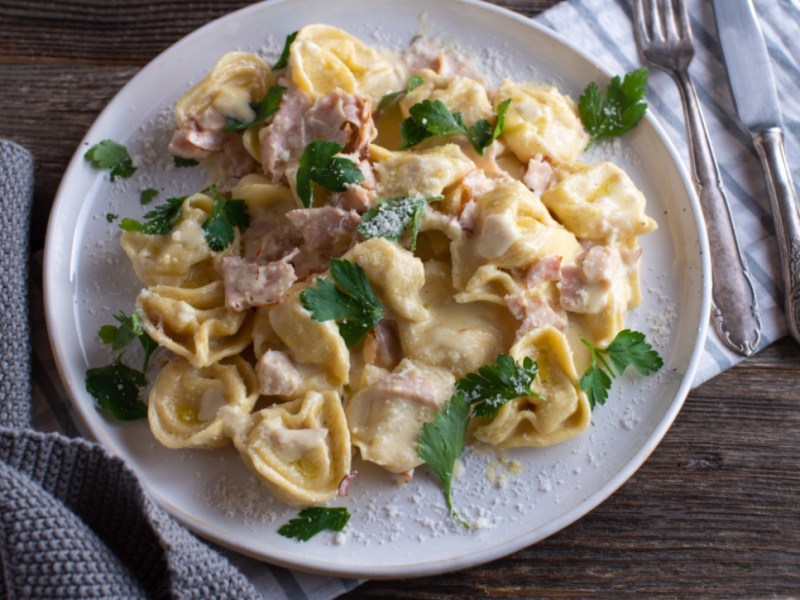 Eine Portion Tortellini alla panna auf einem weißen Teller. Besteck liegt daneben.