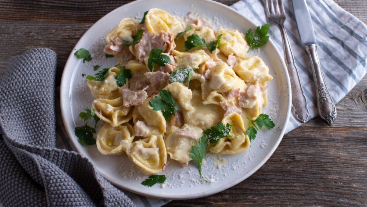 Eine Portion Tortellini alla panna auf einem weißen Teller. Besteck liegt daneben.