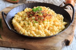 Eine gusseiserne Pfanne vegane Käsespätzle mit Röstzwiebeln und Petersilie, Nahaufnahme.