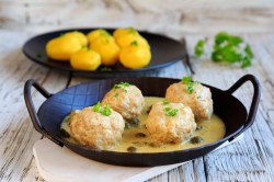 Vegane Königsberger Klopse in einer gusseisernen Pfanne mit Kapernsauce, dazu Salzkartoffeln.