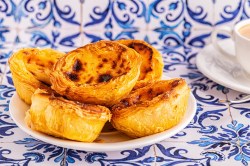 Ein Teller vegane Pastéis de Nata auf typischen blauen portugiesischen Fliesen.