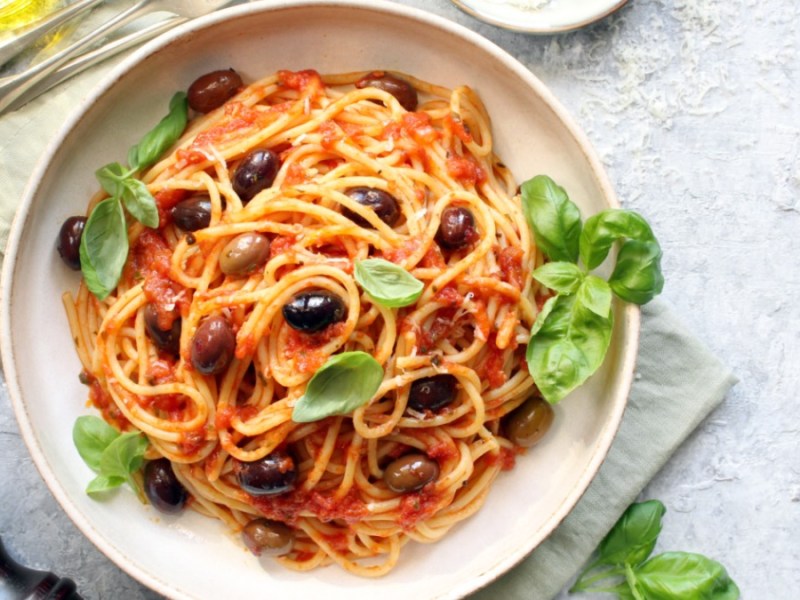 Ein Teller vegane Spaghetti Diavolo mit Oliven und frischem Basilikum.